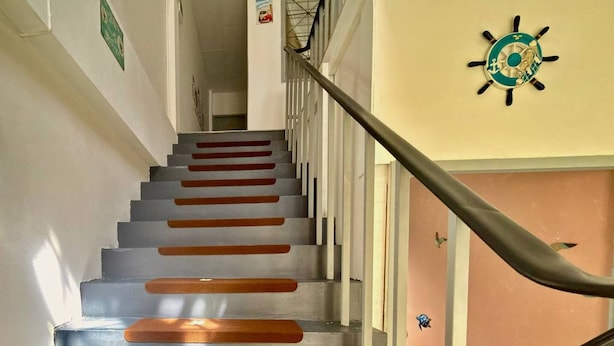 Eine Treppe mit Holzbodenstufen und einem Metallgeländer, die zu einer Zwischenebene mit einem festmontierten Schiffssteuer führt.