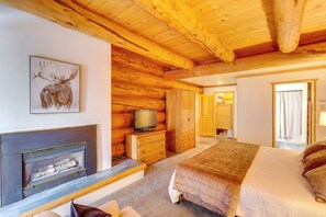 A log cabin interior with a fireplace, a bed, a television, and a wooden ceiling. - Real Log Cabin in Flagstaff with Forest Views (Flagstaff)