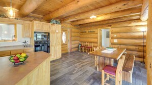 Interior de uma cabana de tronco com cozinha, sala de jantar e um amplo teto de madeira.