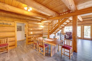 Ein Holzinnenraum mit Essbereich, Stühlen, einem Tisch, einer Treppe und Blick durch eine Tür.