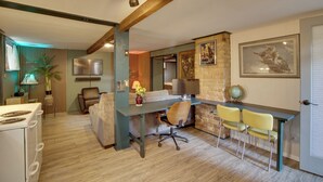 A room with a wooden floor, a desk with a chair, a sofa, a TV, and a lamp.