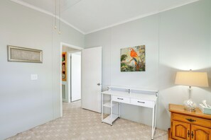 Ein Zimmer mit weißem Schreibtisch, Holzschrank, Papageienbild und einem gerahmten Schild an der Wand.