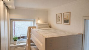 Habitación con literas, ventana, radiador y dos cuadros en la pared.