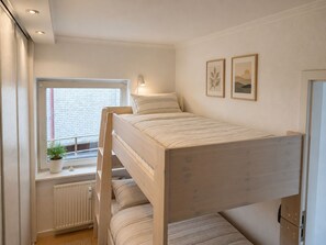 Ein Schlafraum mit Etagenbetten, einem Fenster, einem Heizkörper und zwei gerahmten Bildern an der Wand.