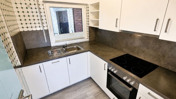 Una cocina moderna con armarios blancos, un lavamanos de acero inoxidable, horno empotrado y una ventana con persianas.