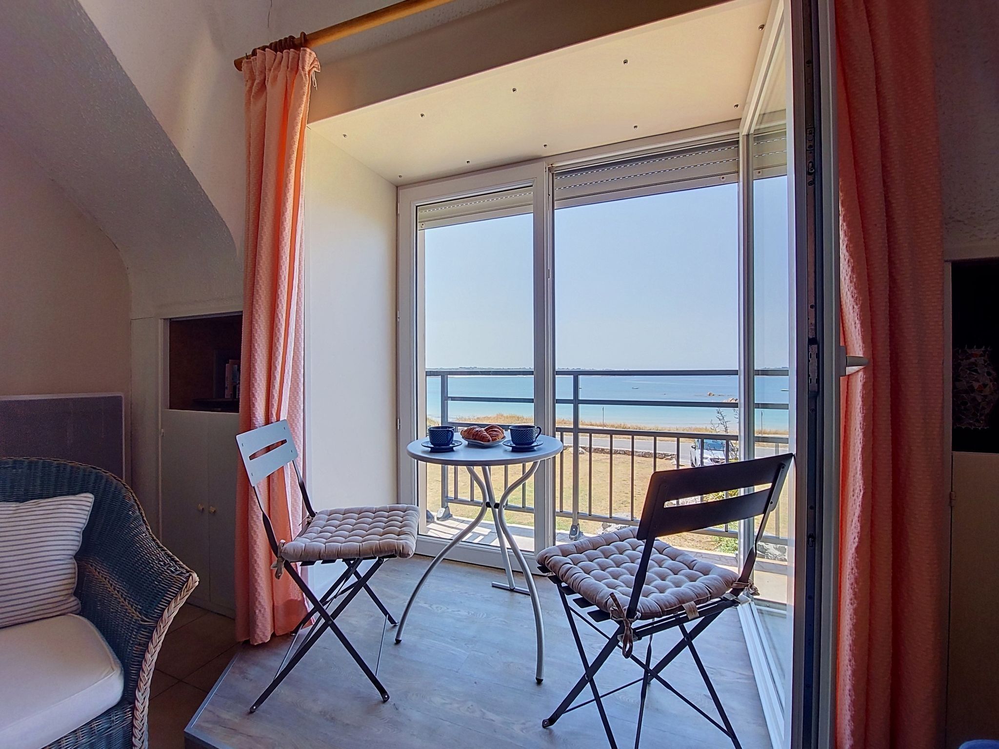 A balcony with two chairs, a small table, and a view of the sea.