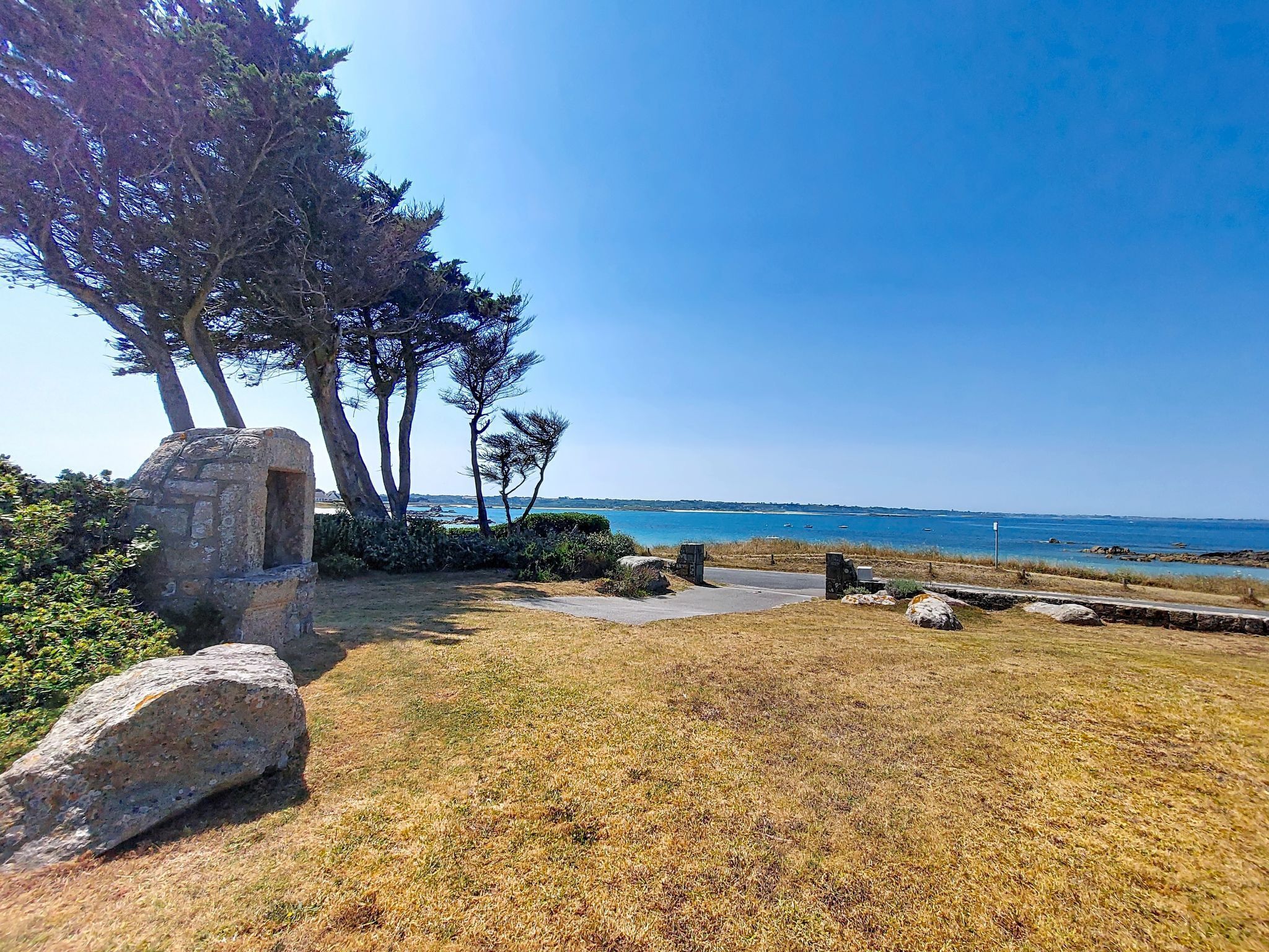 Un paysage côtier avec une structure en pierre, des arbres et une vue dégagée sur la mer.