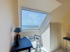 A room with a skylight, a table with a lamp, a chair, and a wardrobe.
