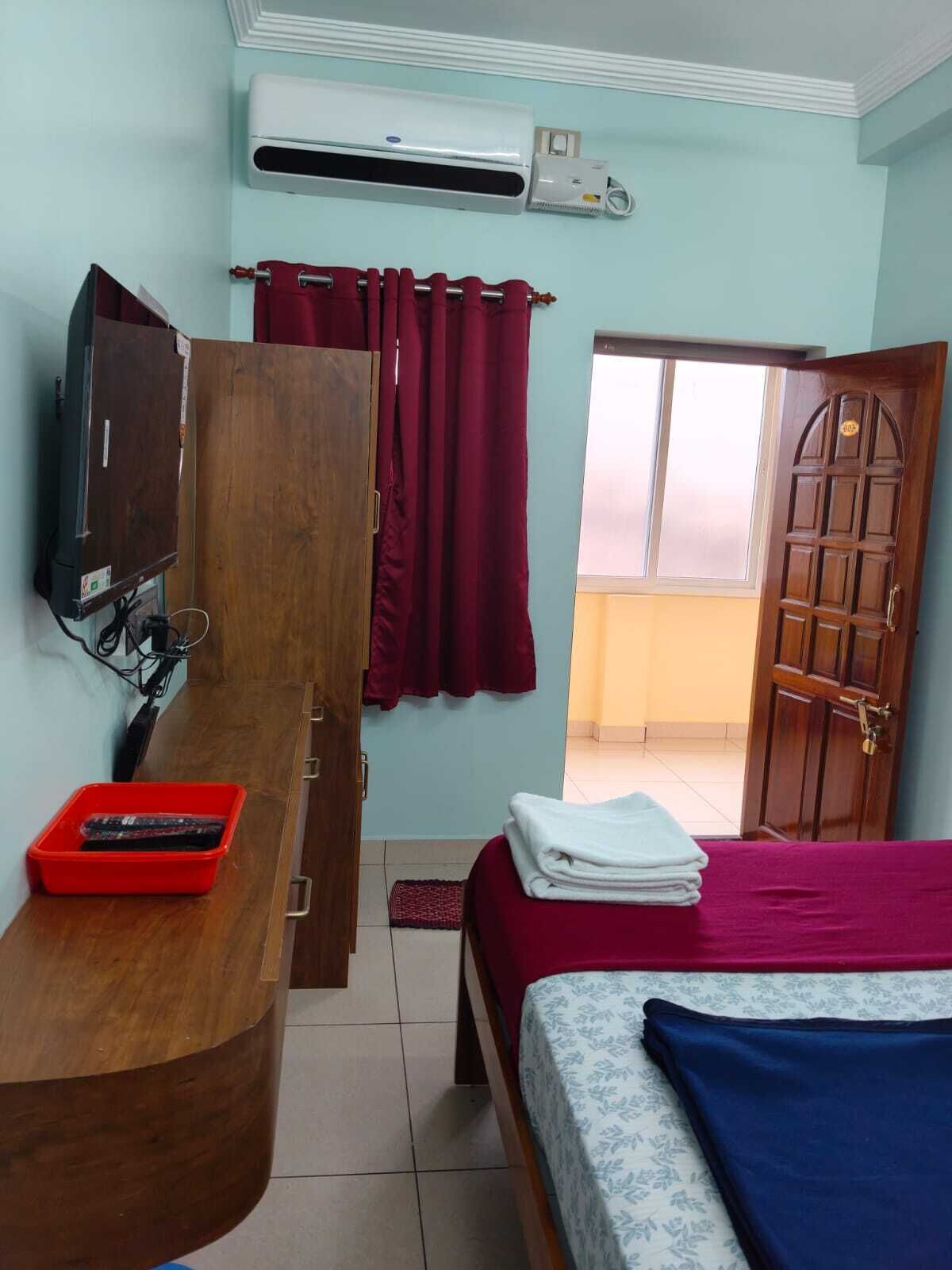 Quarto com cama, escrivaninha de madeira com televisão, ar condicionado e cesto vermelho.