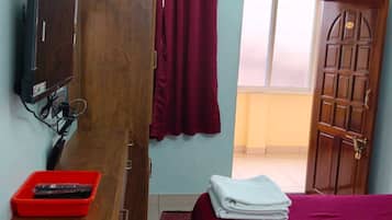 Quarto com cama, escrivaninha de madeira com televisão, ar condicionado e cesto vermelho.