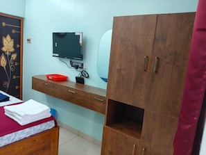A bedroom with a bed, a wooden wardrobe, a TV, and a desk with a mirror. - Malar Residency (Thirunallar)