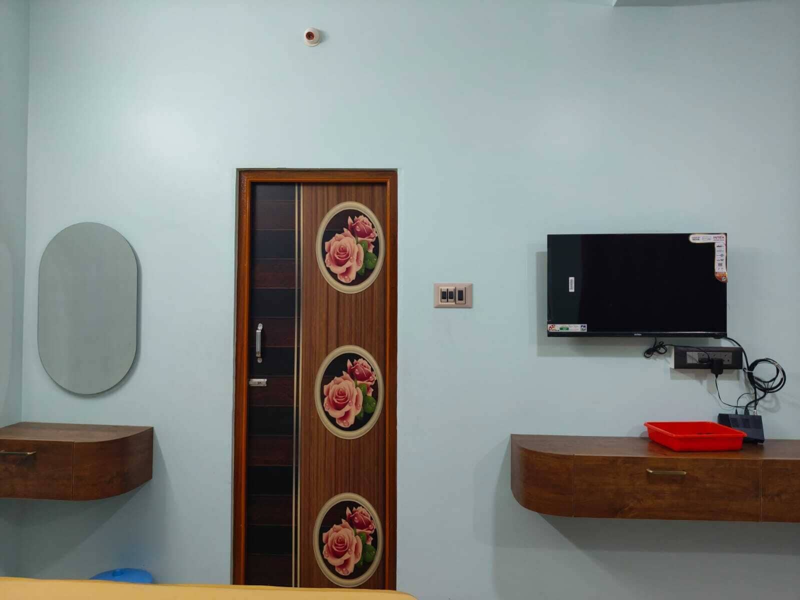 Una habitación con puerta de madera con diseños florales, un televisor montado y armarios de madera con cajones.