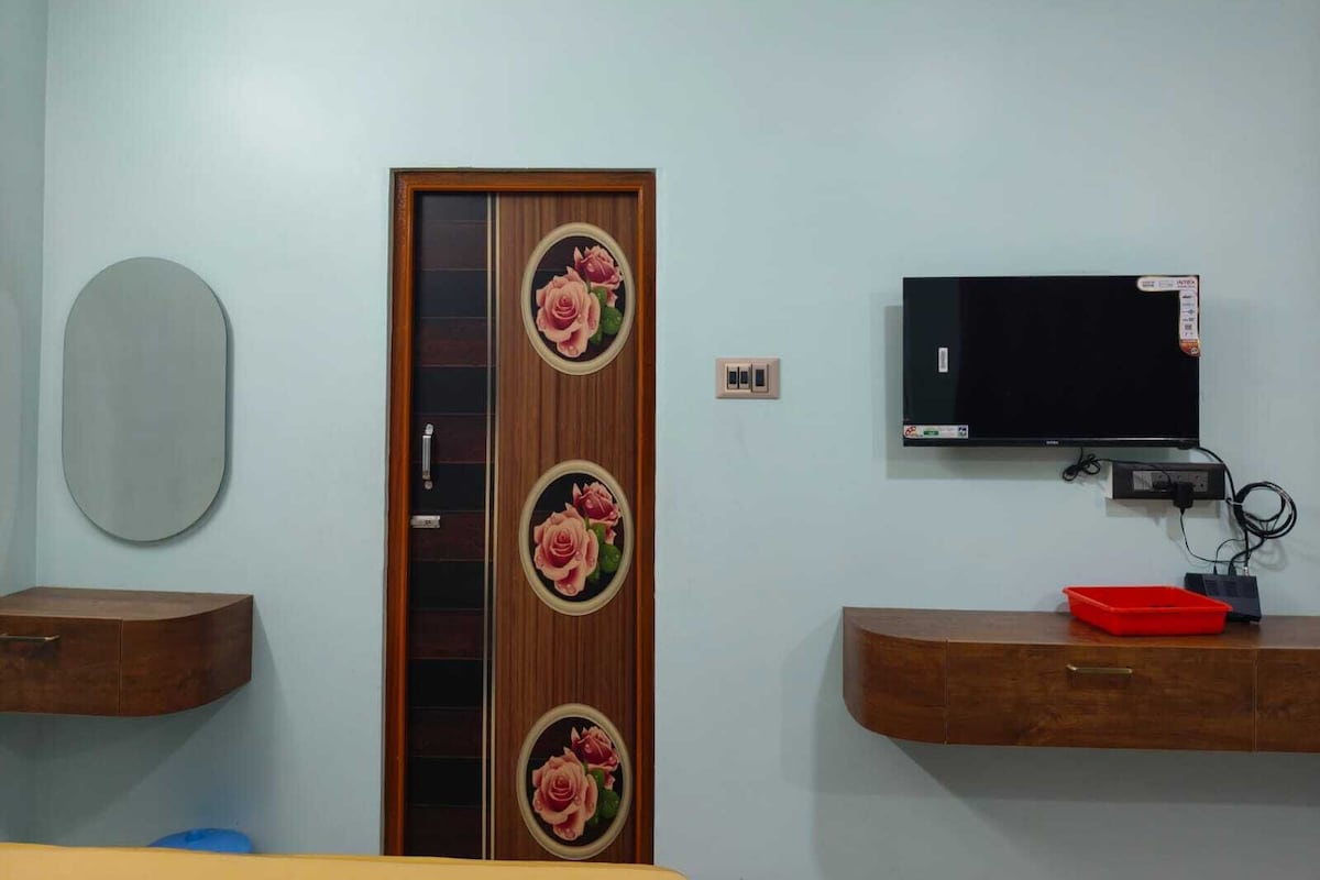 A room with a wooden door with floral designs, a mounted television, and wooden cabinets with drawers.