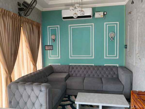 Una sala de estar con un sofá seccional, un sillón capitonado, una mesita blanca y paneles decorativos en la pared.