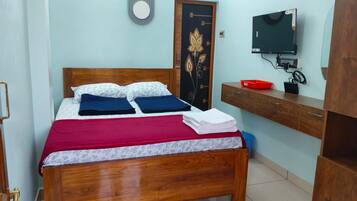 Un dormitorio con una cama de madera, un televisor sobre un mueble de madera, una puerta con diseño floral y una pequeña bandeja roja sobre un aparador de madera.