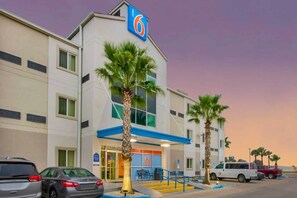 A 6-story hotel with a blue and white facade, palm trees in front, and cars parked outside.