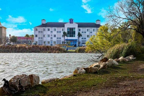 A hotel with a large building, a body of water in the foreground, and a clear sky.