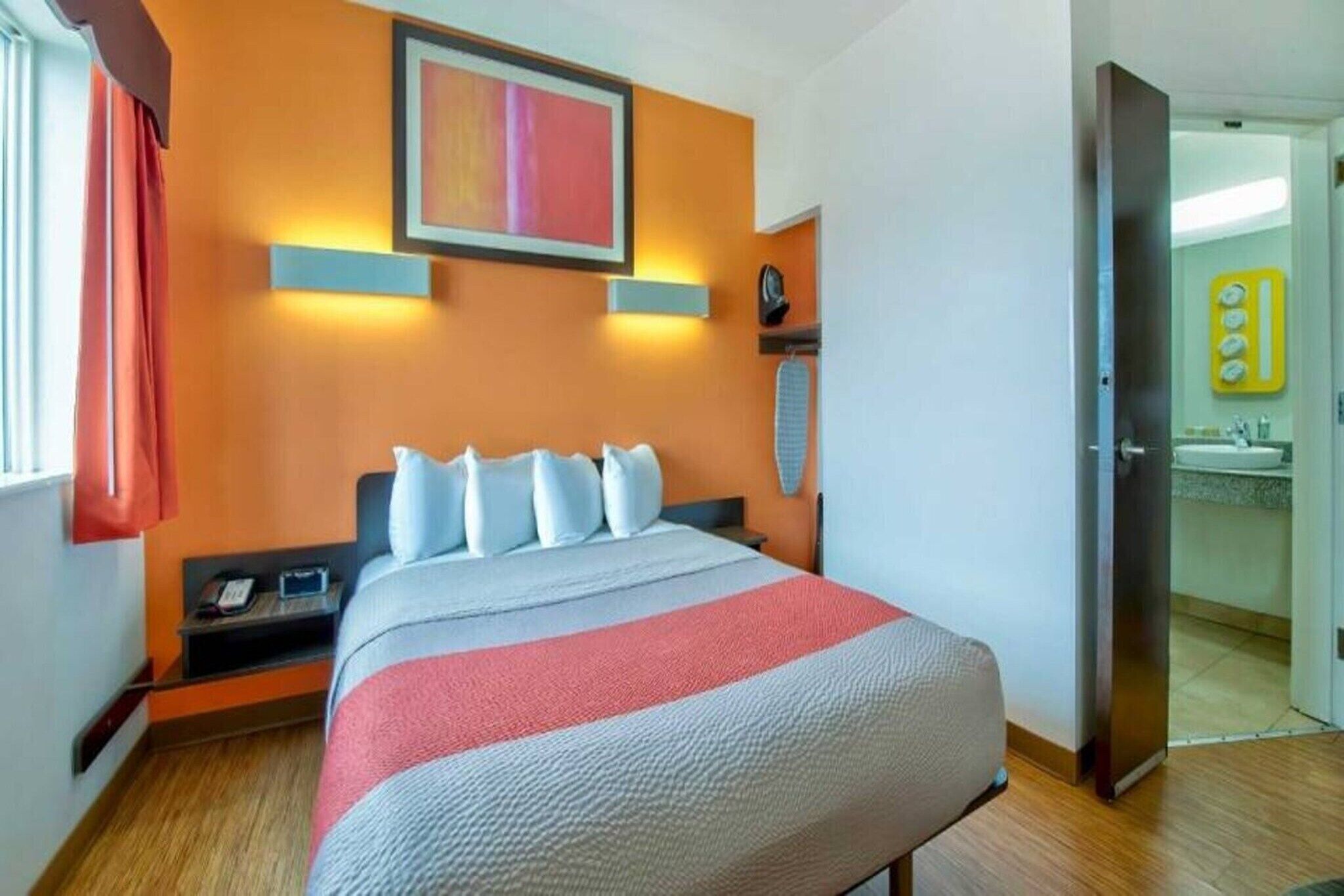 Quarto de hotel com cama, mesa de cabeceira, aquecedor fixado na parede e banheiro visível através de uma porta aberta.