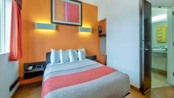 Quarto de hotel com cama, mesa de cabeceira, aquecedor fixado na parede e banheiro visível através de uma porta aberta.