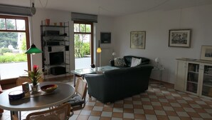 Uma sala de estar com um sofá verde, uma mesa de jantar com cadeiras, um radiador e uma estante de livros.