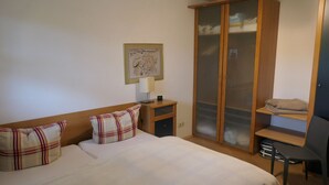 Um quarto com uma cama, mesa de cabeceira, guarda-roupa, escrivaninha e uma cadeira.