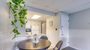 Et spiseområde med et rundt bord, stole, en hængende plante og udsigt til et køkken.