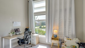 Ein Schlafzimmer mit Schreibtisch, Stuhl, Bett und einem Fenster mit Vorhängen.