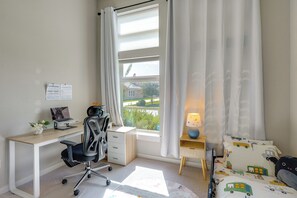 Ein Schlafzimmer mit Schreibtisch, Stuhl, Bett und einem Fenster mit Vorhängen.