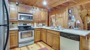 A kitchen with wooden cabinets, a microwave, stove, dishwasher, granite countertop, and a clock on the wall. - Hot Tub & Game Room! Wooded Retreat in Blue Ridge (Blue Ridge)