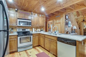 A kitchen with wooden cabinets, a microwave, stove, dishwasher, granite countertop, and a clock on the wall. - Hot Tub & Game Room! Wooded Retreat in Blue Ridge (Blue Ridge)
