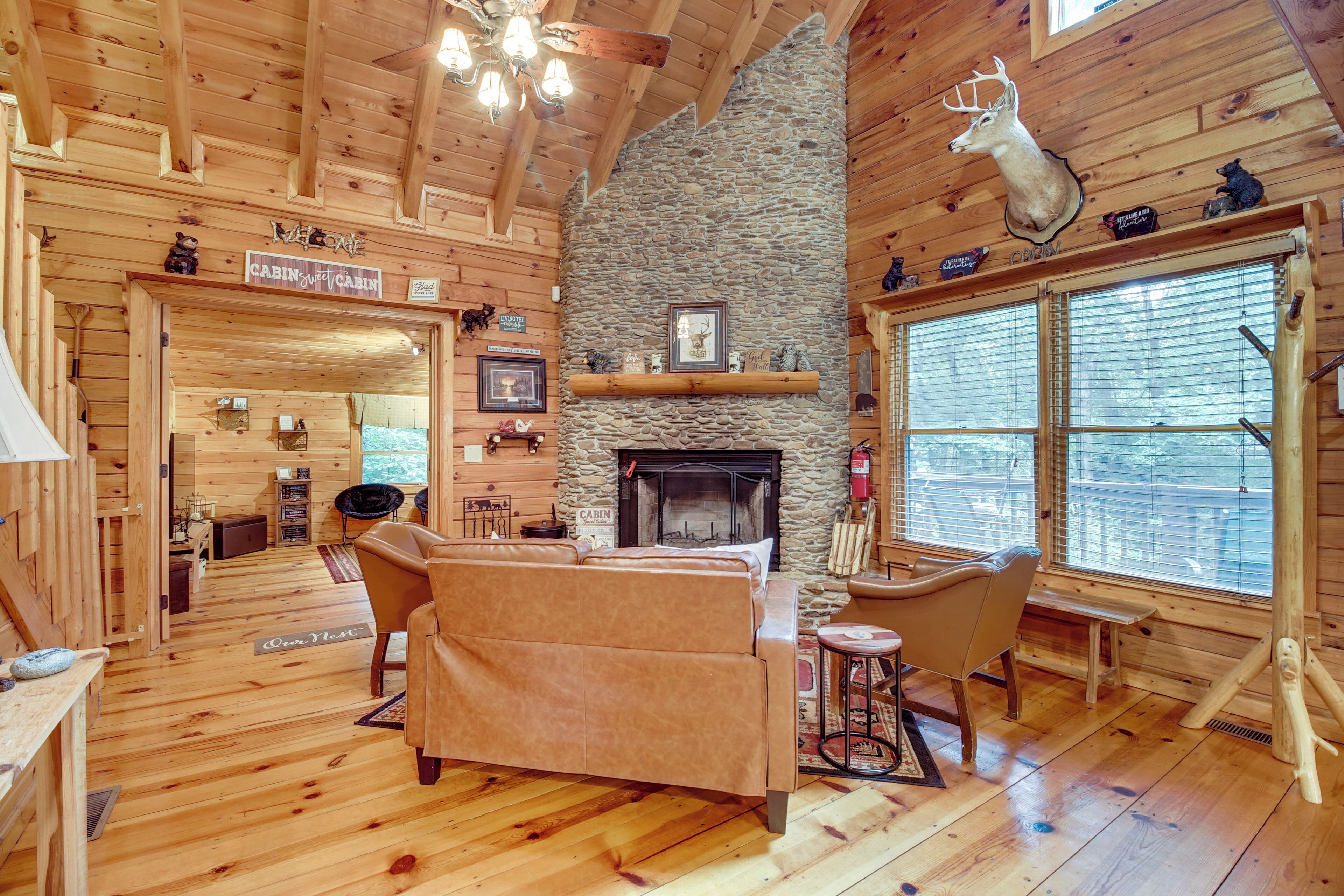 A cabin interior with a stone fireplace, wooden walls, a sofa, and a deer head mounted on the wall.