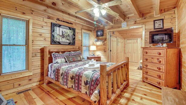 A wooden cabin bedroom with a bed, dresser, ceiling fan, and television. - Hot Tub & Game Room! Wooded Retreat in Blue Ridge (Blue Ridge)