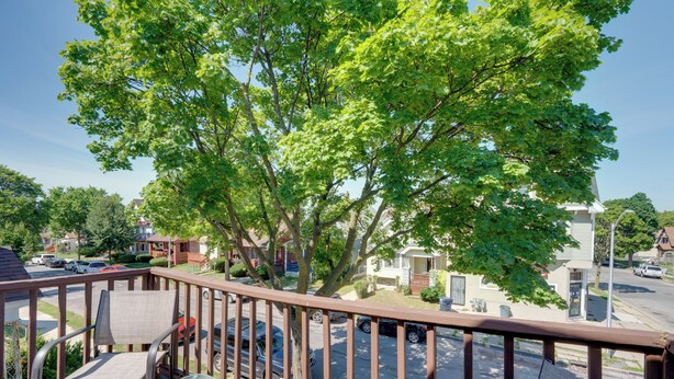 Un balcone con vista su una strada residenziale, un albero e un'auto parcheggiata.