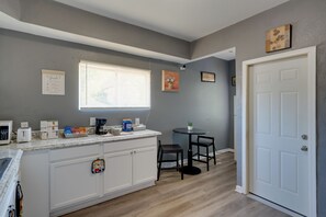 A kitchen with a white countertop, a window with blinds, a small round table with two chairs, and a door.