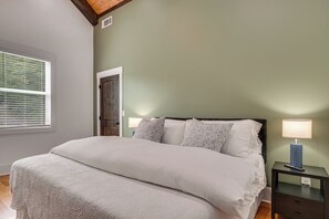 Ein Schlafzimmer mit einem großen Bett, zwei Nachttischlampen, einem Nachttisch und einem Fenster mit Jalousien.