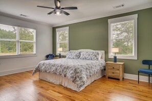 Ein Schlafzimmer mit einem Bett, zwei Nachttischen, einem Deckenventilator und großen Fenstern.