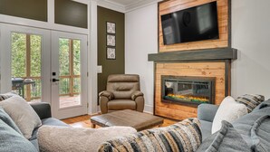 A living room with a fireplace, a television mounted above it, and a comfortable seating area with a sofa and a chair. - Luxe 4BR Cabin at Innsbruck Resort in Helen (Helen)
