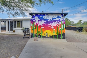 Une maison dont la façade extérieure est ornée d’une fresque colorée, avec une porte de garage et un pot de fleurs placé sur l’allée.
