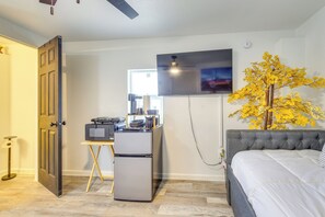 Une chambre à coucher de taille réduite, comprenant un lit, un bureau avec un réfrigérateur, une télévision et une plante décorative.