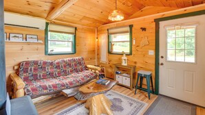 A cozy cabin interior with a wooden floor, a patterned sofa, a coffee table, and a door with a window.