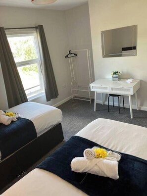 A hotel room with two beds, a desk, a mirror, and a window with curtains.
