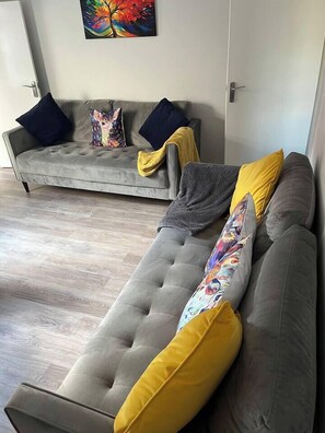 A modern living room with a grey sofa and a grey sofa bed, both with multiple pillows.