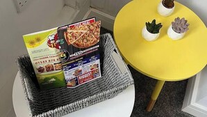 Eine Ecke des Raumes mit einem weißen Tisch, einem gelben Tisch und einem Korb voller Pizzakartons.