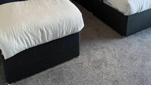 Ein Hotelzimmer mit zwei Betten, beide mit weißer Bettwäsche und dunklen Kopfteilen. Dazwischen befindet sich ein Nachttisch mit einer Lampe.