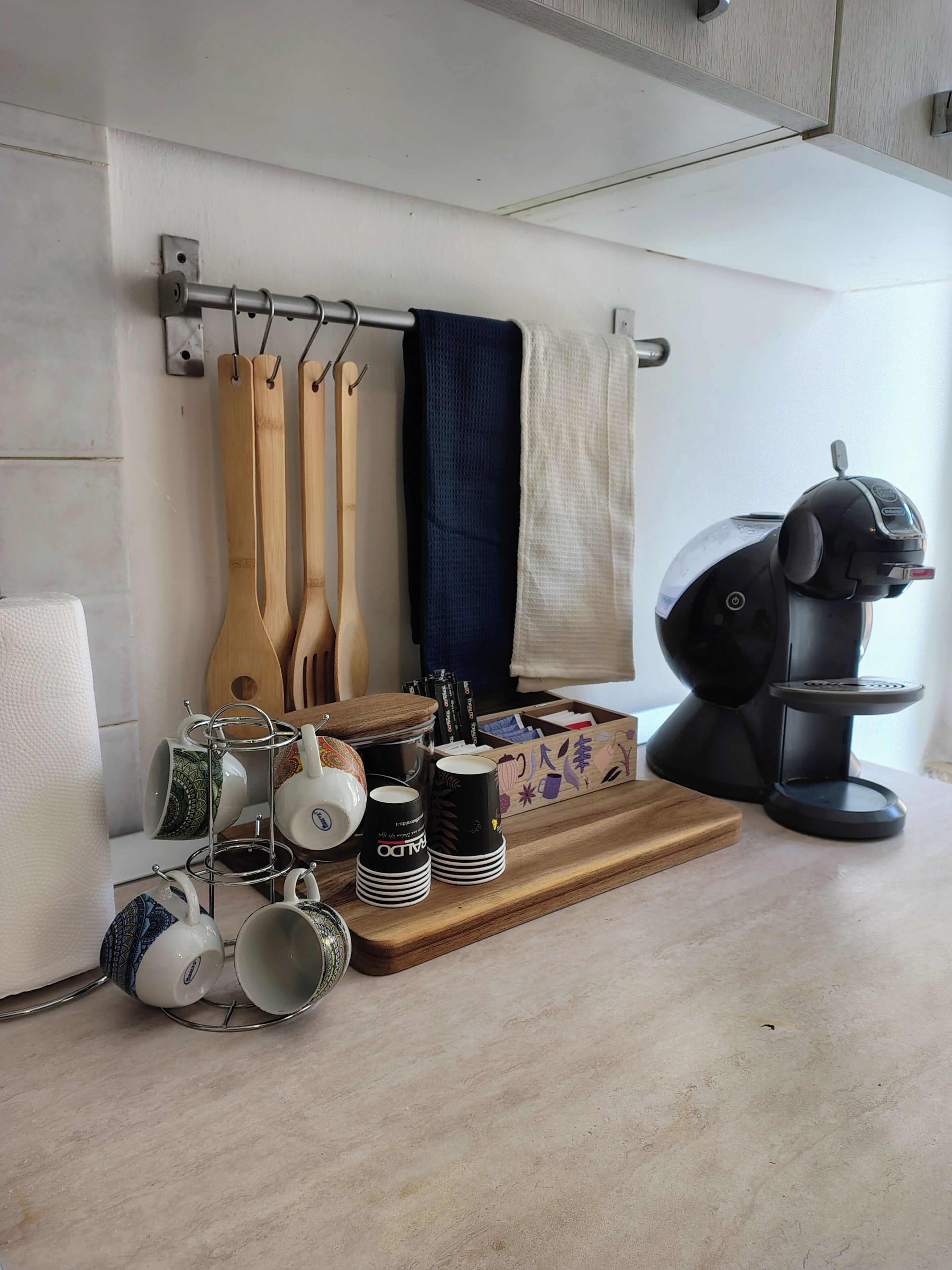 A kitchen with a coffee maker, wooden utensils, and a tray with mugs and teapots.