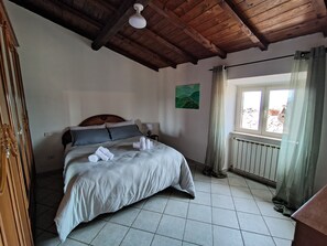 A bedroom with a bed, a wooden ceiling, a window with curtains, and a radiator.