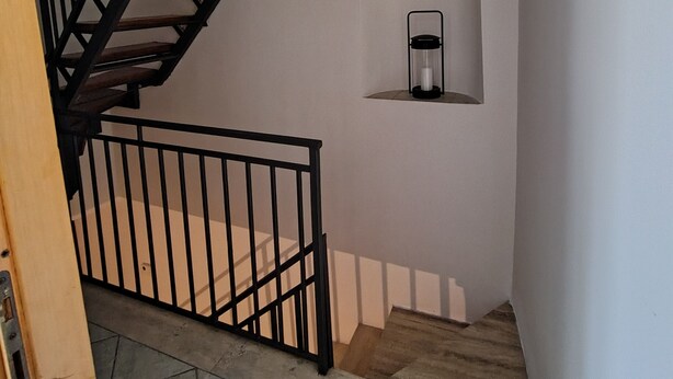 A staircase with a wooden handrail and black balusters, a black pendant light, and a small shelf with a candle. - Your home in the historic center of Alatri - 2 bedrooms and 2 bathrooms - pets allowed (Alatri)