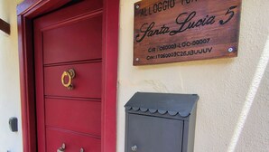 A red door with a brass handle, a wooden sign above it, and a small mailbox on the wall. - Your home in the historic center of Alatri - 2 bedrooms and 2 bathrooms - pets allowed (Alatri)