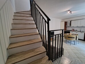 A staircase with wooden steps and black railings leading to a kitchen area with white cabinets and a dining table. - Your home in the historic center of Alatri - 2 bedrooms and 2 bathrooms - pets allowed (Alatri)