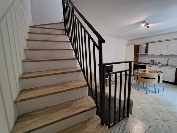 A staircase with wooden steps and black railings leading to a kitchen area with white cabinets and a dining table.